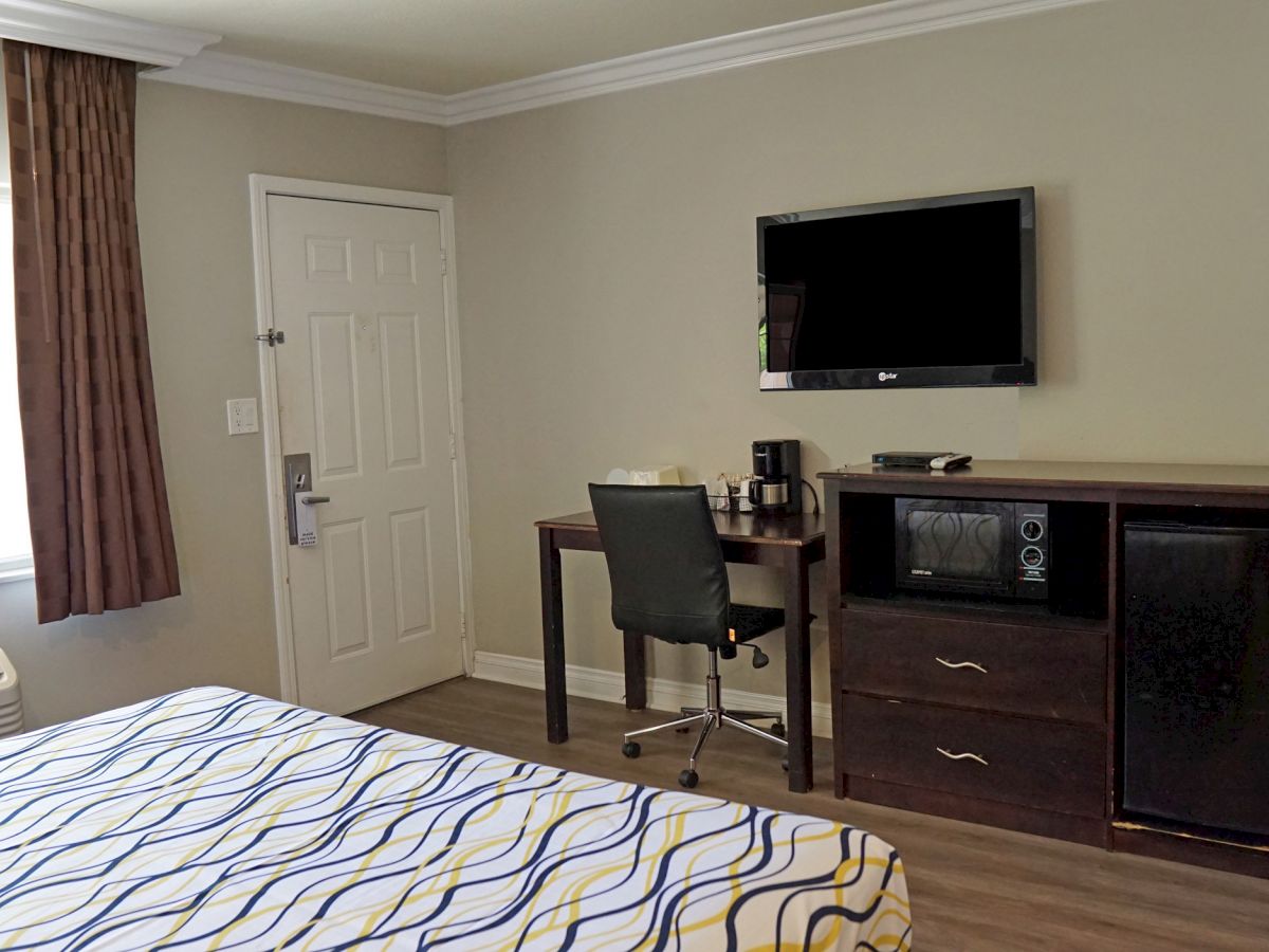 A hotel room with a bed, desk, chair, TV, minibar, microwave, and coffee maker. There's also a window, door, and air conditioner in the room.