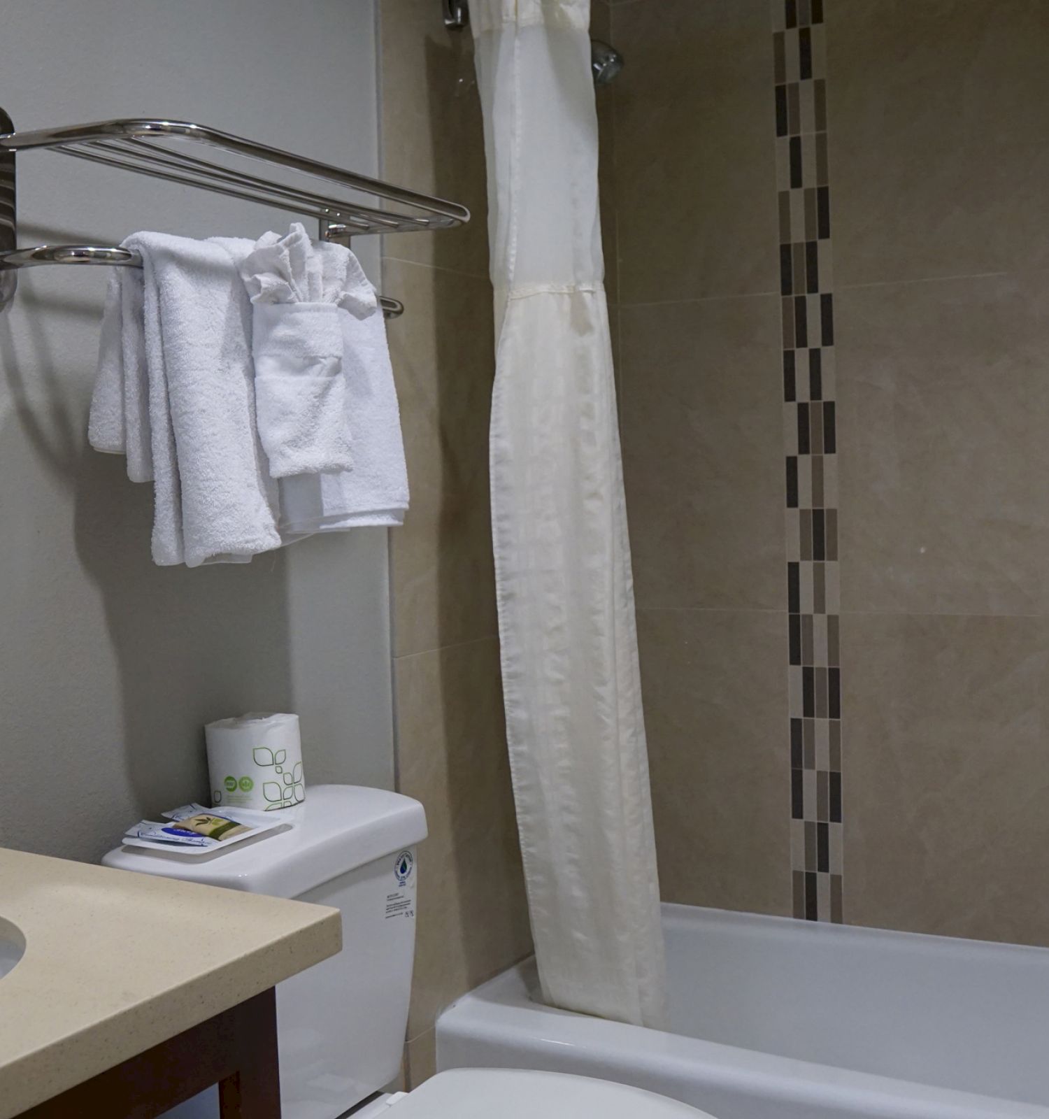 This image shows a clean bathroom with a sink, a mirror, a towel rack with white towels, a toilet, and a bathtub with a shower curtain drawn.