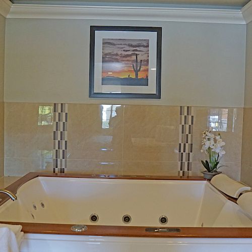 This image shows a modern bathroom with a white spa bathtub, a rolled towel, a small vase with flowers, and a framed picture on the wall.