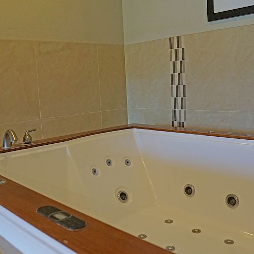 This image shows a jacuzzi-style bathtub with jets and wooden trim, set in a tiled bathroom. There are folded towels on the side.