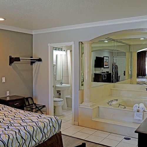 A hotel room featuring a bed, a bathroom, a large mirrored whirlpool tub, a TV, and a dresser.